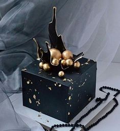 a black box with gold ornaments on it and a chain attached to the side, sitting on a white surface