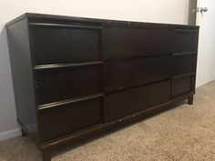 an empty room with a brown dresser and carpeted flooring in front of a white wall