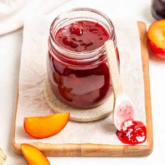 a glass jar filled with jam sitting on top of a cutting board next to sliced fruit