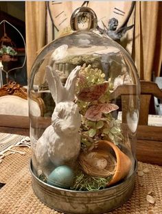 a glass cloche with some plants and eggs in it on top of a table