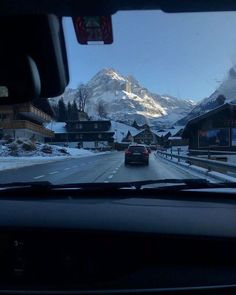 a car is driving down the road in front of some snow covered mountains and houses