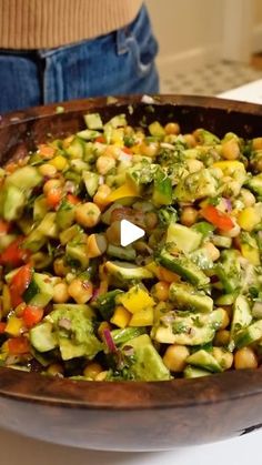 a wooden bowl filled with vegetables on top of a counter next to a woman's stomach