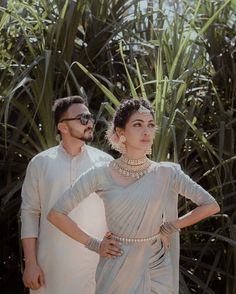 a man and woman standing next to each other in front of palm trees wearing white outfits