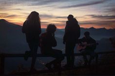 three people standing on top of a mountain at sunset