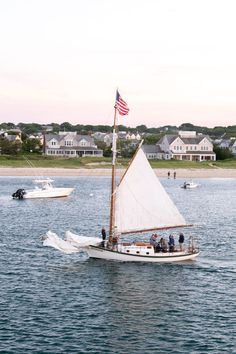 a sailboat with people on it in the water near some houses and an american flag