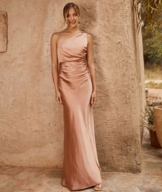 a woman standing in front of a stone wall wearing a pink one - shoulder dress