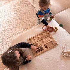 two young children playing with wooden toys on the floor in front of a couch and rug