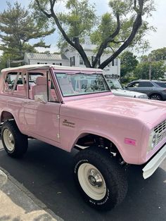 an old pink truck parked in a parking lot next to some trees and other cars