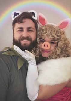 a man and woman dressed up as pigs posing for a photo with a rainbow in the background