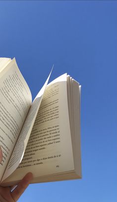 an open book being held up in the air by someone's hand, against a blue sky