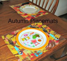 a wooden table topped with a plate covered in children's artwork and utensils