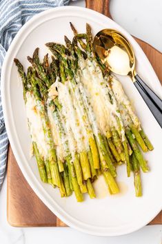 asparagus with parmesan cheese on a white plate next to a spoon