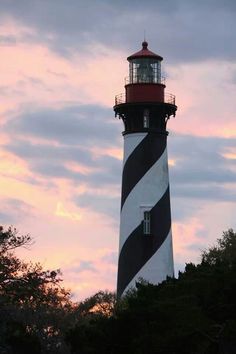 a black and white striped lighthouse with trees in the foreground against a cloudy sky