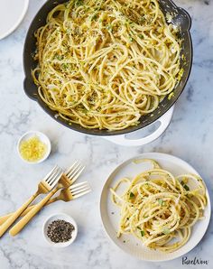 pasta in a skillet on a marble table with two plates and spoons next to it