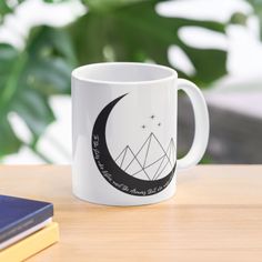 a white coffee mug sitting on top of a wooden table next to a book and plant