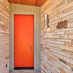 an orange door is on the side of a brick building with a light fixture above it