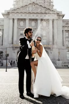 a bride and groom pose for a photo in front of an old building with fountain