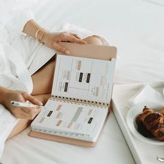 a woman is sitting on her bed with a planner and pen in front of her