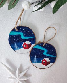 two christmas ornaments hanging from strings on a white surface with snowflakes and greenery