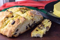 a loaf of bread sitting on top of a wooden table next to a plate with a piece of cake