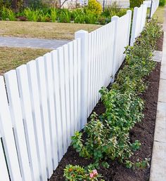 a white picket fence next to a flower bed