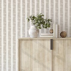 a white vase sitting on top of a wooden cabinet next to a wallpapered wall