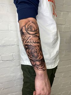 a man's arm with roses and the word blossom tattooed on it, in front of a brick wall