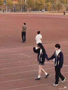 two people holding hands walking across a tennis court with another person in the distance on one side