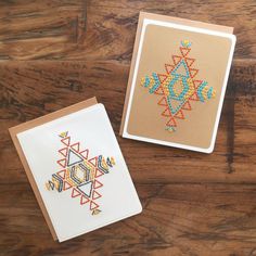 two cards with designs on them sitting on top of a wooden table next to each other