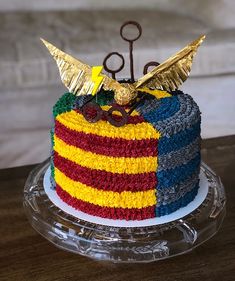 a multi - colored cake with gold accents and scissors on top is sitting on a clear plate