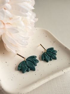 two pairs of green leaf shaped earrings on a white plate next to a large flower