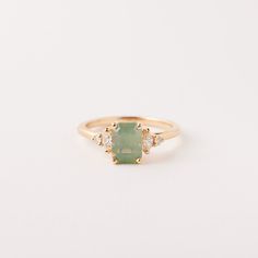 a gold ring with an emerald stone and three diamonds on the side, sitting on a white surface