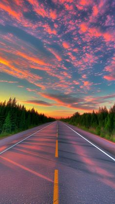 an empty road with trees in the background and colorful clouds above it at sunset or dawn