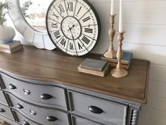 a clock on top of a dresser next to a mirror and candle holders with books