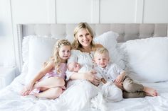 a woman and two children are sitting on a bed with white sheets in the background