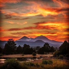 the sun is setting over mountains and trees