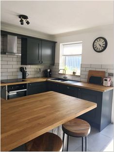 a kitchen with black cabinets and wooden counter tops, two stools in front of the sink