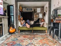 two people laying on a couch in a living room with guitars hanging from the wall