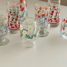 several glass cups are lined up on a table with flowers painted all over the sides