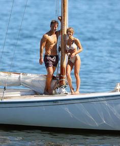 two people standing on the front of a sailboat in the water, with one person leaning against the mast