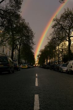 two rainbows are seen in the sky over a street lined with parked cars and trees