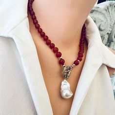 Add a bohemian flair to your collection with this red agate toggle necklace, featuring a beautiful baroque pearl pendant for an elegant contrast. The deep red orangy agate beads are hand-knotted, showcasing artisanal craftsmanship and providing durability and flexibility. The necklace is accented with gold-filled and gold bronze details, adding a touch of warmth and luxury to the design. Measuring 18.5 inches, this piece is perfect for layering or wearing on its own as a statement. MATERIALS: Re Luxury Red Necklace With Pearl Pendant, Elegant Red Necklace With Large Beads, Handmade Luxury Red Pearl Necklace, Luxury Red Pearl Pendant Necklace, Red Necklaces With Polished Oval Beads, Luxury Handmade Red Pearl Necklace, Red Necklaces With Large Oval Beads, Luxury Red Pearl Pendant Jewelry, Elegant Red Pearl Necklace With Faceted Beads