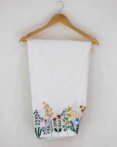 a white towel hanging on a wooden hanger with flowers and plants painted on it