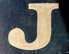 the letter j is carved into wood with white paint and gold lettering on black background