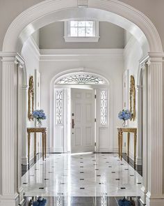 an elegant entry way with marble floors and white walls, blue flowers on either side of the door