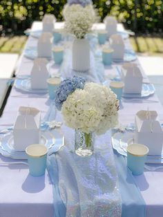 the table is set with blue and white flowers in vases, napkins, and cups