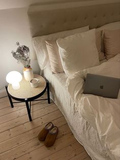 a laptop computer sitting on top of a bed next to a night stand and lamp