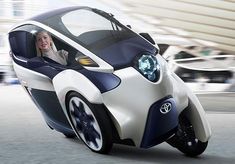 a futuristic car with a woman in the driver's seat is driving down the street