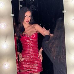 a woman in a short red dress standing next to a mirror with lights on it