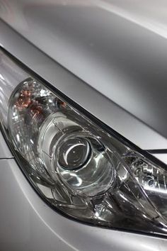 the front end of a silver car with its lights on